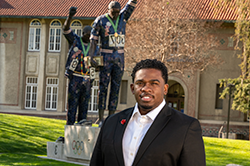 Black male in suit in front of Victory statue on San Jose States campus